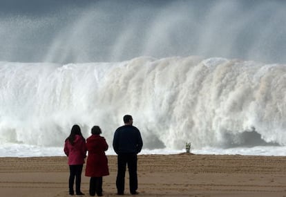 Três pessoas observam uma onda na praia do Meco, onde ocorreu a tragédia.