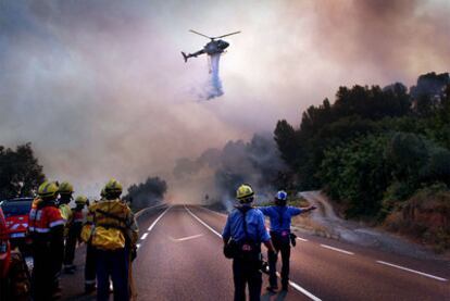 Varios bomberos observan cómo un helicóptero descarga agua sobre el terreno incendiado, ayer en La Riba (Alt Camp).