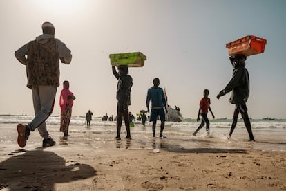 Un grupo de pescadores jóvenes camina hacia el mar para descargar el pescado que acaba de traer una embarcación tradicional de pesca en el puerto de Nuakchot, Mauritania.