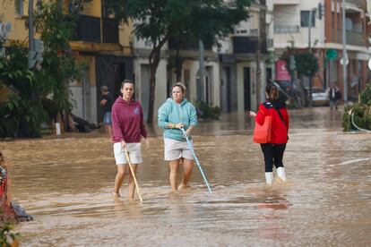 Varias personas cruzan una calle de Sedaví (en la Comunidad Valenciana) anegada a causa de las lluvias torrenciales de las últimas horas.