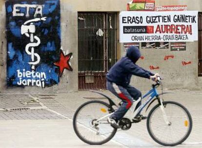 Un joven pasea por un pueblo navarro ante un cartel con el emblema de ETA y otro que dice "Por encima de todos los ataques, ahora el pueblo, ahora la paz".