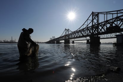 Un trabajador chino recoge basura en el río Yalu, junto al puente que lleva a Corea del Norte.