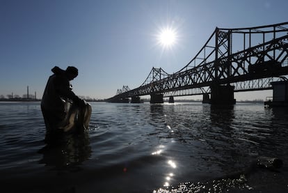 Un trabajador chino recoge basura en el río Yalu, junto al puente que lleva a Corea del Norte.