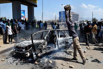 Un hombre lanza una piedra a un coche calcinado durante las protestas de los opositores en Kisumu (Kenia). 