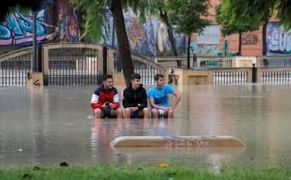 Tres jóvenes permanecen sentados en un banco de un parque inundado en Orihuela (Alicante), este viernes.