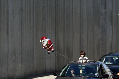 Un niño sostiene un Papa Noel en el convoy que traslada al Patriarca de Jerusalén Fouad Twal a Belén, Cisjordania.