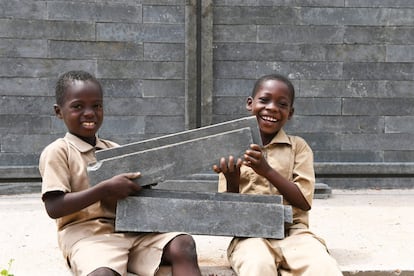 Dos niños sostienen ladrillos de plástico reciclado, que son mucho más livianos que los que están fabricados de cemento u otros materiales, con los que se está construyendo su nuevo colegio en Sakassou.