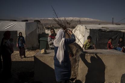 Una mujer introduce leña en el horno que las vecinas como ella utilizan para cocinar la comida en el asentamiento informal Terbol Dalhsmeyeh 052.