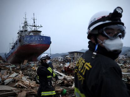 Dos bomberos caminan entre escombros ante un buque arrastrado por el tsunami tierra adentro en Kesennuma.