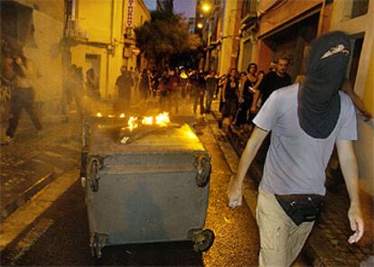 Un joven encapuchado junto a un contenedor ardiendo, anoche, en las calles de Sants.