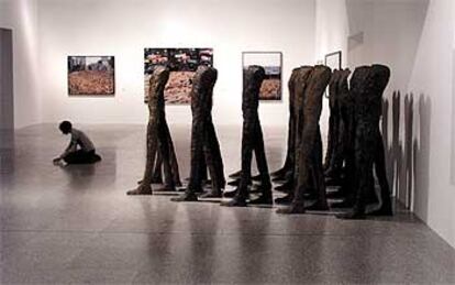 Una joven toma notas en la muestra junto a <i>Caminando</i> (1998-1999), conjunto escultórico de la polaca Magdalena Abakanowicz. Al fondo, tres fotografías del norteamericano Spencer Tunick.