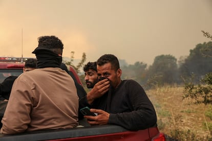 Un hombre se cubre la cara para protegerse del humo mientras es trasladado por los bomberos a un lugar seguro con otros migrantes rescatados de las llamas en Evros (Grecia) este viernes.

