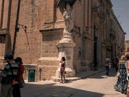 Mdina, Malta. 12 de mayo de 2018. Una joven se detiene un momento en una esquina a los pies de una imagen de la Virgen y el Niño. Por todo el país hay numerosas figuras de María parecidas a esta, tanto en las esquinas de las calles como en las casas. La Virgen ocupa un lugar destacado en las creencias religiosas de los malteses. En la fe católica, ella dio a luz a Jesús, hijo de Dios.