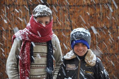 Dos niños, abrigados con gorros y bufandas, posan en medio de una nevada.