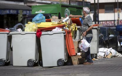 Un hombre intenta depositar sus bolsas de basura en unos contenedores ya llenos en la calle Saavedra Fajardo, cerca del Paseo de Extremadura.