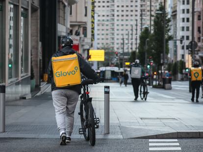 Dos repartidores de Glovo y otro de Deliveroo caminan por la Gran Vía de Madrid, en abril.