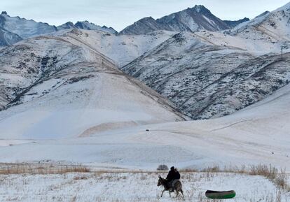Dos niños montan en un burro que remolca una balsa inflable en un sendero cubierto de nieve cerca del pueblo de Kyzyl Birlik, a unos 25 km de Biskek (Kirguistán).
