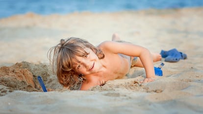 Un niño en la playa metiendo un brazo en un hoyo.