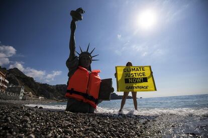 Una activista de Greenpeace muestra una pancarta junto a una reproducción de la Estatua de la Libertad, con chaleco salvavidas y semienterrada, en la playa de Giardini Naxos, cerca de Messina, Sicilia, de cara a la celebración de la cumbre del G7 en Taormina (Italia).