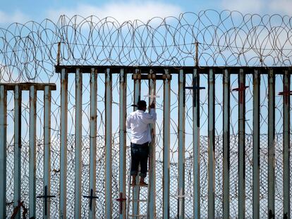 Josue Serrano, un mexicano deportado de EE UU, coloca una cruz sobre el muro fronterizo en Tijuana.