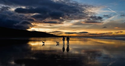 Una pareja camina junto a sus perros en la playa al atardecer en el Equinoccio de Otoño, que marca el primer día de otoño en Saltburn, Inglaterra.