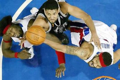Tim Duncan, de los Spurs, salta por el balón entre dos rivales de los Pistons.