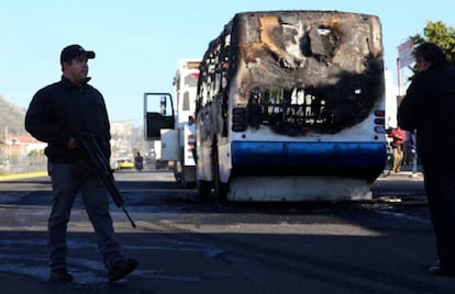 Un polic&iacute;a junto a uno de los autobuses incendiados durante un operativo en contra del CJNG en la ciudad de Zapopan en 2014.