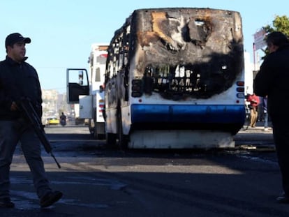 Un polic&iacute;a junto a uno de los autobuses incendiados durante un operativo en contra del CJNG en la ciudad de Zapopan en 2014.