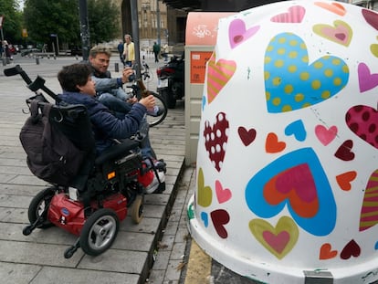 Dos personas en silla de ruedas tratan de depositar envases de vidrio en un contenedor personalizado por Agatha Ruiz de la Prada en Vitoria.