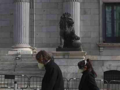 Dos transeúntes caminan frente al Congreso de los Diputados protegidos con mascarillas.