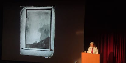 Anne Carson, durante su conferencia, y con una fotografía antigua en blanco y negro donde parecen apreciarse dos pájaros.