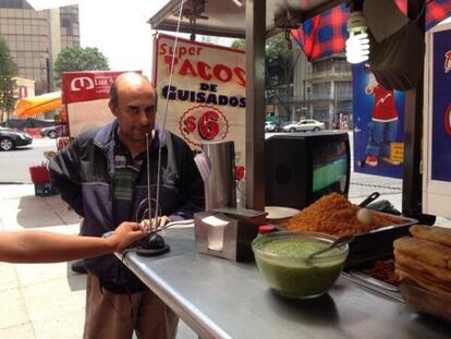 Un hombre espera ser atendido en un puesto de tacos en la capital de México, a un lado de un televisor que transmite el partido entre la selección mexicana y Brasil.