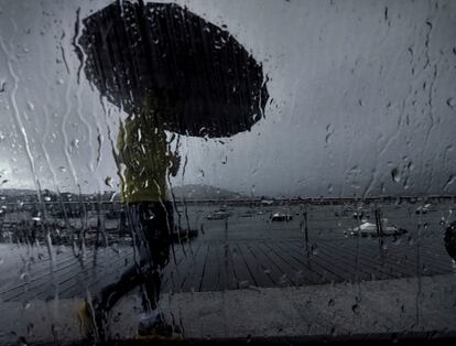 Un hombre con paraguas caminaba este lunes por el puerto coruñés de Pontedeume, en una jornada marcada nuevamente por las lluvias.