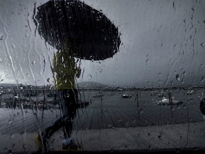Un hombre con paraguas caminaba este lunes por el puerto coruñés de Pontedeume, en una jornada marcada nuevamente por las lluvias.