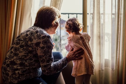 Una abuela mira por la ventana junto a su nieta.