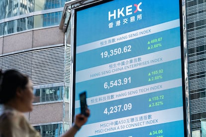 Una mujer usa su móvil frente a una pantalla digital que muestra los números del índice Hang Seng, en la plaza de la Bolsa de Hong Kong, China, en una imagen de archivo.