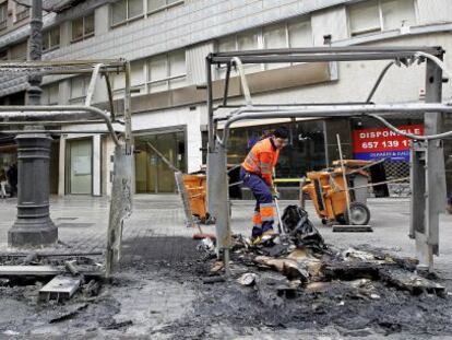 Una trabajadora retira en la avenida de Bar&oacute;n de C&aacute;rcer de Valencia los restos de dos contenedores quemados.