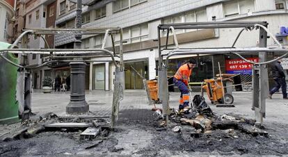 Una trabajadora retira en la avenida de Bar&oacute;n de C&aacute;rcer de Valencia los restos de dos contenedores quemados.