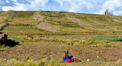 Una ‘cholita’ se sienta entre los campos de quinoa de la población de Puerto Pérez. Al fondo, uno de los tanques que el programa de abastecimiento de agua del Gobierno, el BID y la Aecid.
