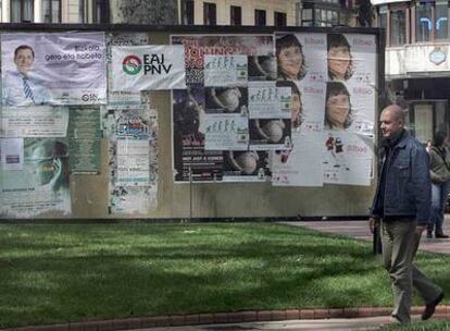 Una persona pasea ante un panel lleno de carteles electorales de los partidos en el centro de Bilbao.