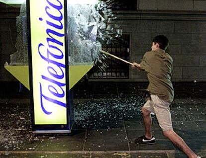 Arriba, un joven argentino destroza una cabina de teléfonos.