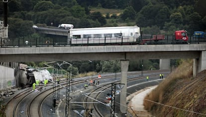 Operarios continúan trabajando en la curva donde descarriló el tren Alvia, mientras un camión se lleva uno de los vagones siniestrados, 26 de julio de 2013.