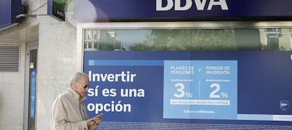 Una persona pasa delante de una sucursal en la que se anuncian planes de pensiones.