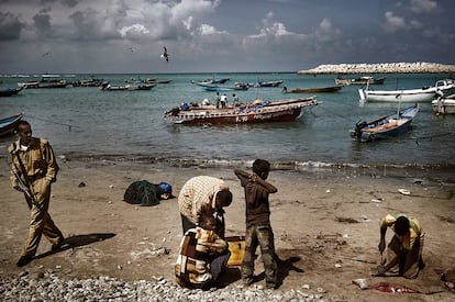 Jvenes somales cortan pescado en la playa de Bosaso bajo la mirada de un guardia de seguridad; la imagen fue tomada el 21 de noviembre de 2008.