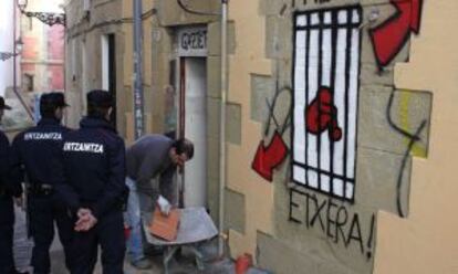 Dos agentes observan a un operario mientras tapia el acceso al 'gaztetxe' Uxotegi, en San Sebastián.