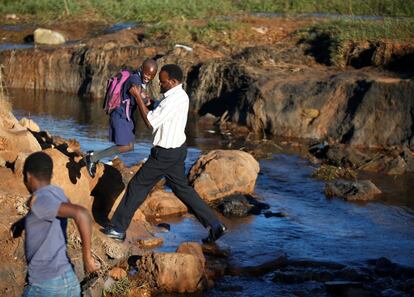 John Manake, padre y voluntario, ayuda a los niños a cruzar un puente peatonal temporal de camino a la escuela de primaria Pagomo, en Chipigne (Zimbabue), tras el paso del ciclón Idai.