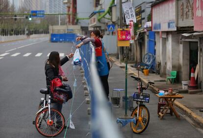 En esta fotografía del pasado 16 de marzo una mujer entrega una bolsa con comida por encima de una valla. Las autoridades chinas utilizaron este sistema para separar zonas de la ciudad de Wuhan y evitar la propagación de la epidemia.