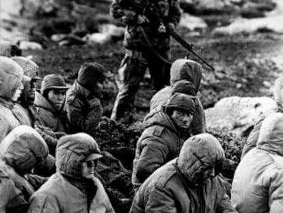 A Royal Navy officer guards Argentinean prisoners during the 1982 Falklands War.