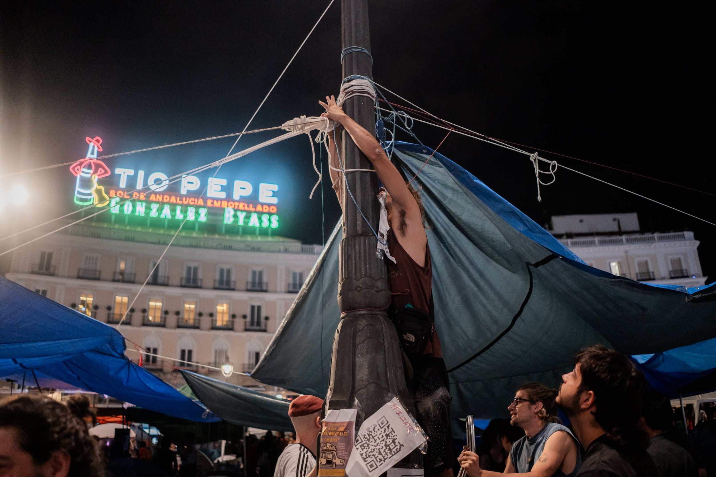 Un joven instala una lona para resguardar de la lluvia a los manifestantes durante la segunda noche de la acampada en la Puerta del Sol, en Madrid.