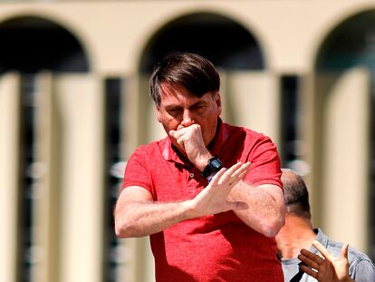 Brazilian President Jair Bolsonaro coughs as he speaks after joining his supporters who were taking part in a motorcade to protest against quarantine and social distancing measures to combat the new coronavirus outbreak in Brasilia on April 19, 2020. (Photo by Sergio LIMA / AFP)